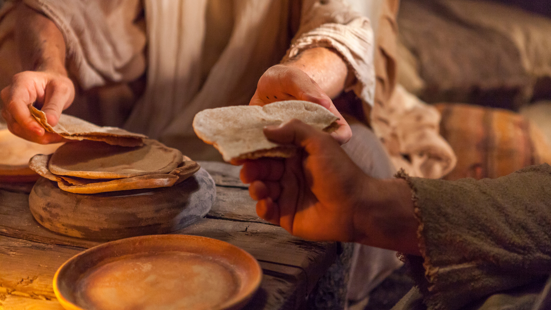 A person breaks bread and hands it to someone. Bread is one example of Passover imagery Jesus Christ used in his "Bread of Life" sermon.